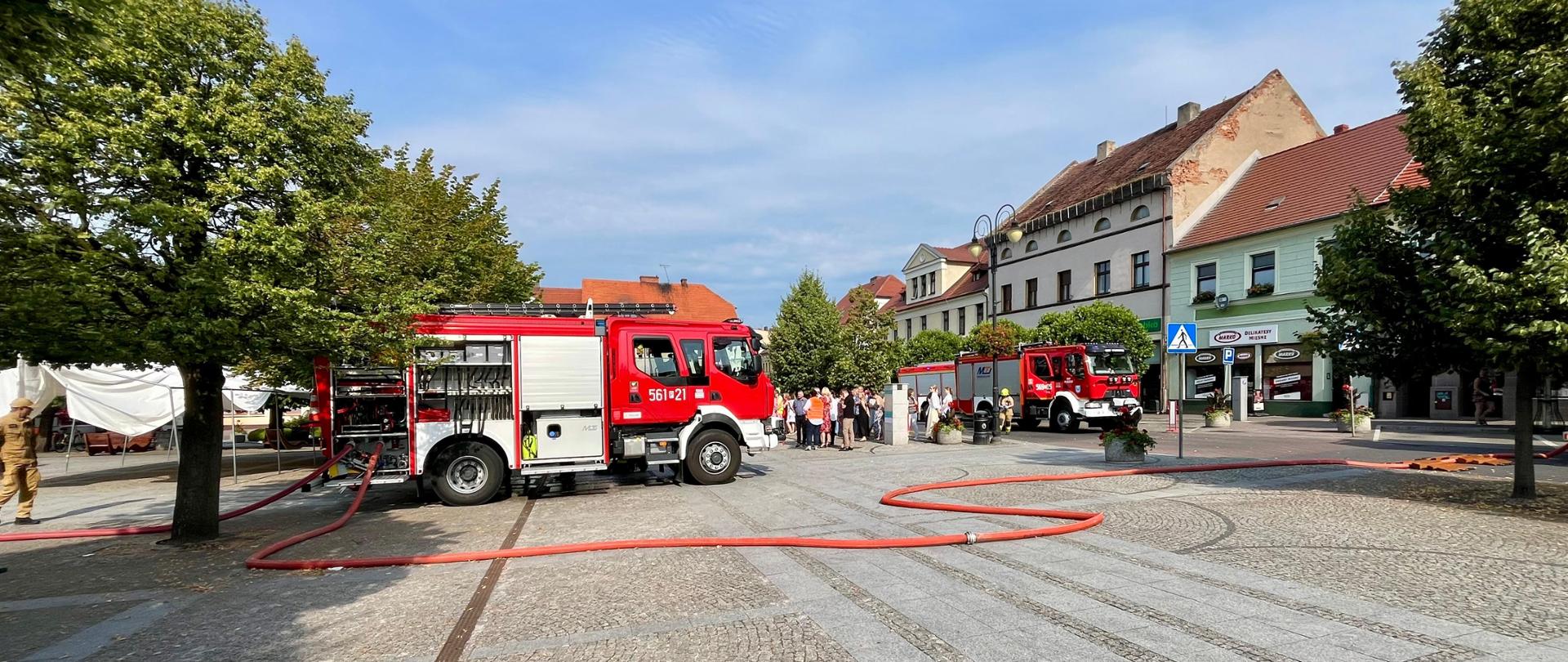 dwa czerwone pojazdy strażackie ustawione przodem do siebie na pleszewskim rynku, w tle pracownicy urzędu