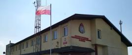 Zdjęcie przedstawia strażaków na tle budynku komendy.