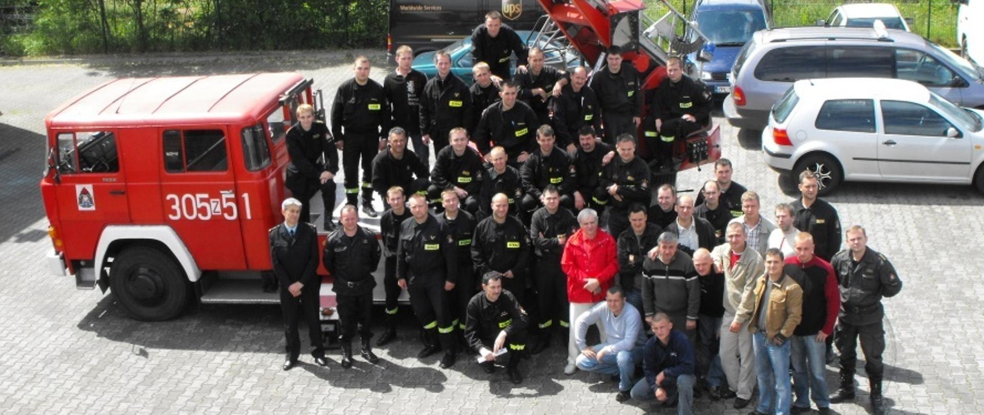 Egzaminatorzy oraz strazacy na tle drabiny mechanicznej