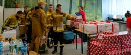 Strażacy w siedzibie akcji Szlachetna Paczka sortują otrzymane od darczyńców paczki, które przekazane zostaną potrzebującym, w tle wolontariusze akcji.