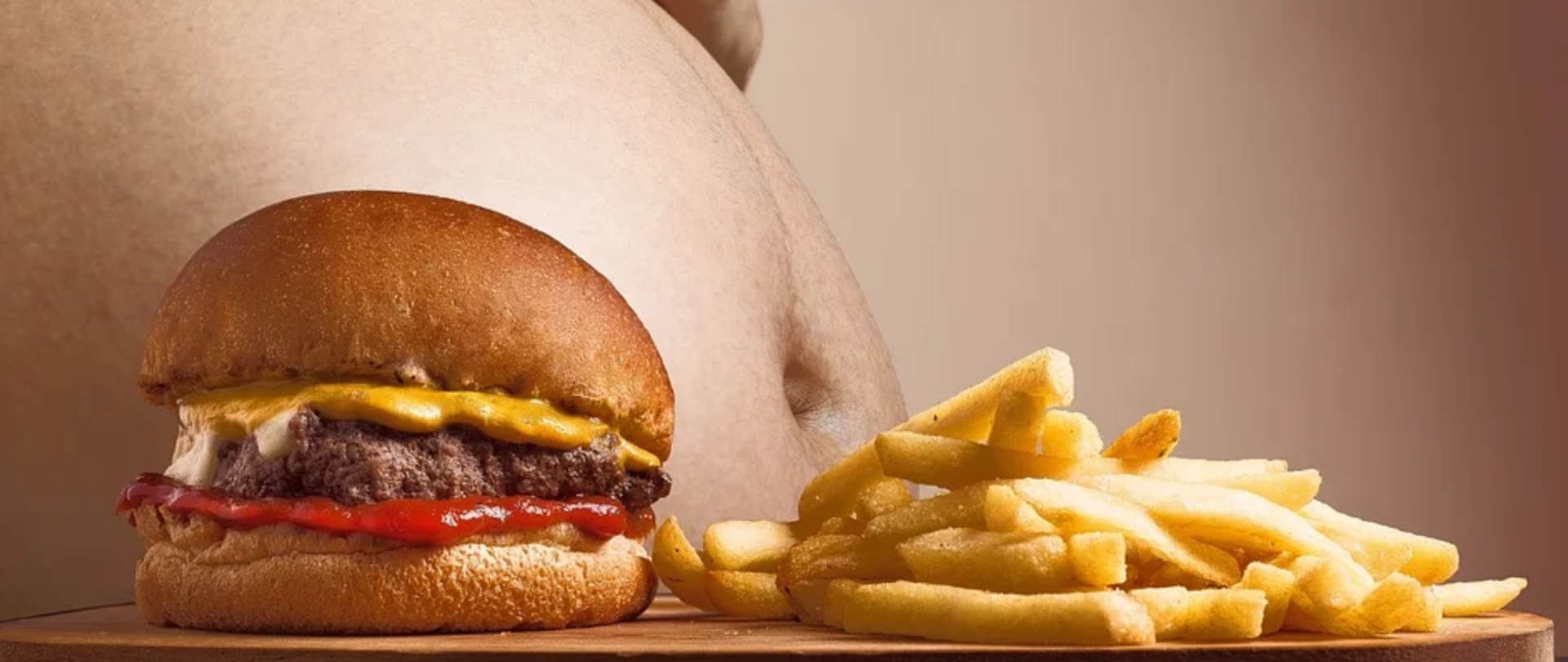 Obraz przedstawia duży brzuch otyłej osoby, przed którym na okrągłej desce wyeksponowany jest hamburger, obok leży porcja frytek
