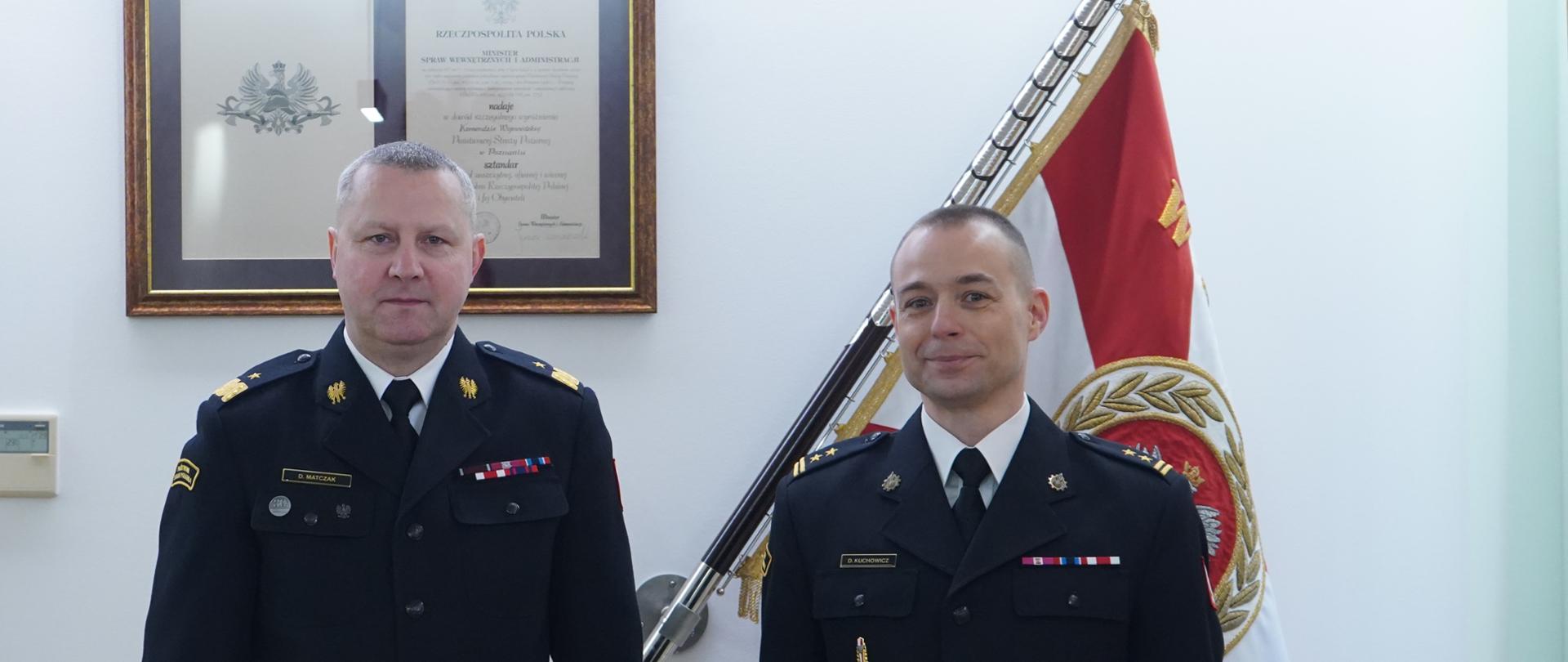 dwóch strażaków stoi obok siebie, w tle sztandar