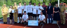 Kolorowa fotografia wykonana w pogodny dzień na zewnątrz. Przedstawia strażaków sportowców po wręczeniu medali i nagród w sporcie pożarniczym . Z boku komendant i osoby wręczające.