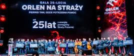 Uczestnicy i laureaci gali „ORLEN na Straży” zgromadzeni na scenie z pamiątkowymi tablicami. W tle ekran z napisem „Od 25 lat z energią pomagamy Straży Pożarnej”.