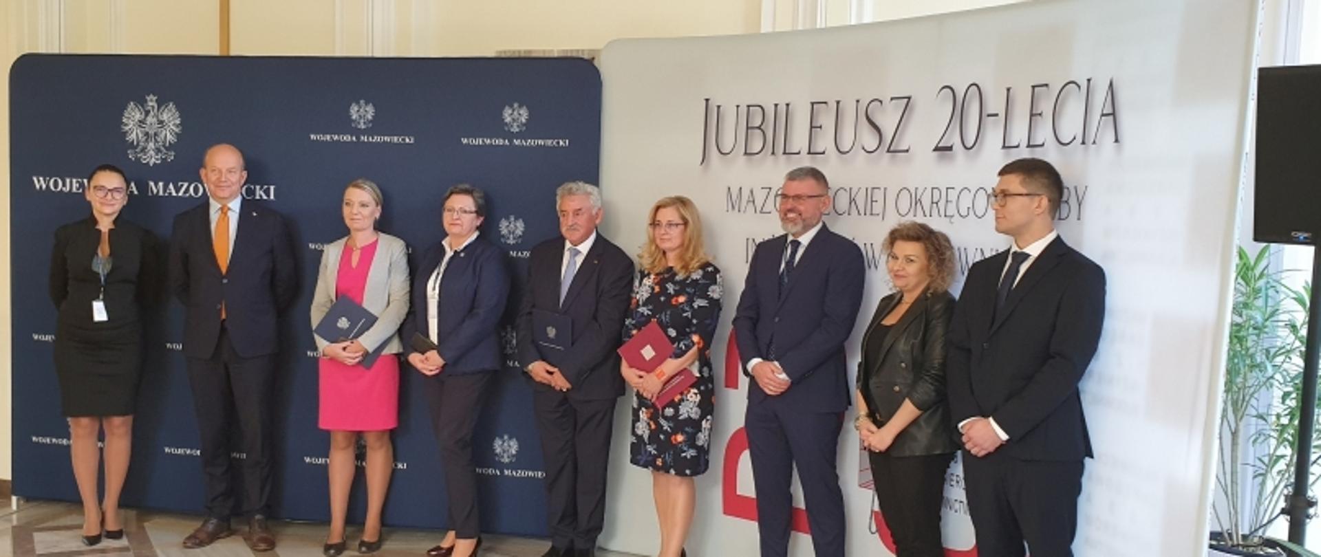 Grupa osób stojąca przed roll-upami z napisami „Województwo Mazowieckie” i „Jubileusz 20-lecia Mazowieckiej Okręgowej Izby Inżynierów Budownictwa”.