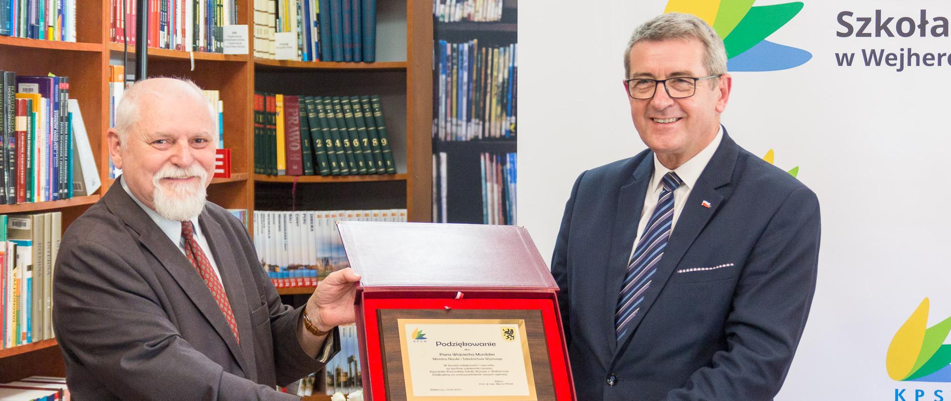 Minister i rektor prezentują ozdobny dokument pozwolenia.