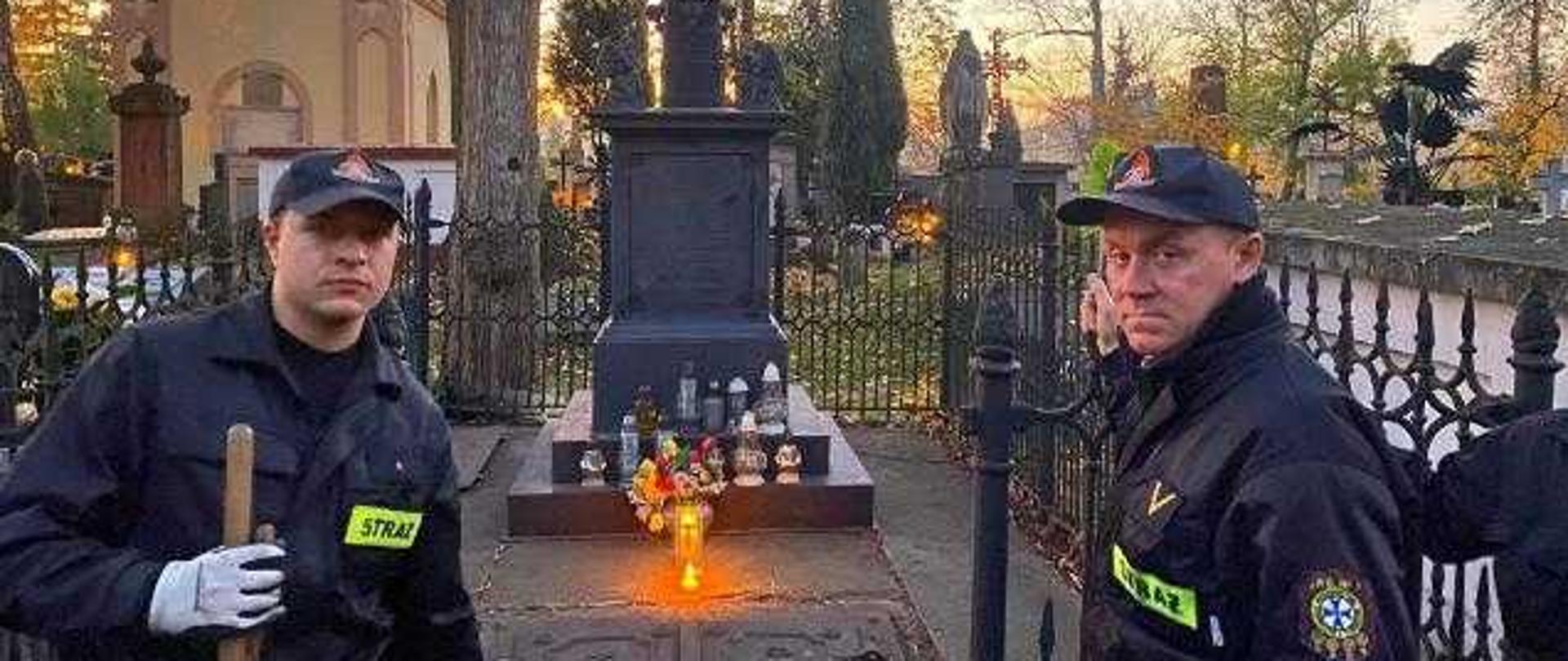 Zdjęcie przedstawia strażaków którzy skończyli porządkować grób. W tle widać zapalony znicz.