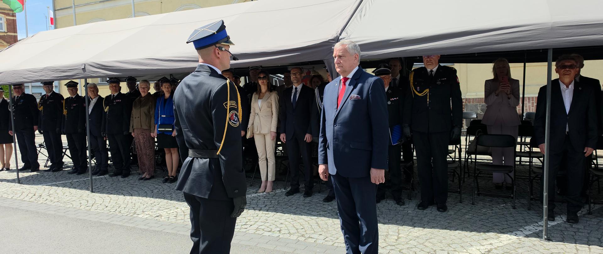 Dowódca uroczystości składa meldunek panu Wiceministrowi. W tle stoją zaproszeni goście.