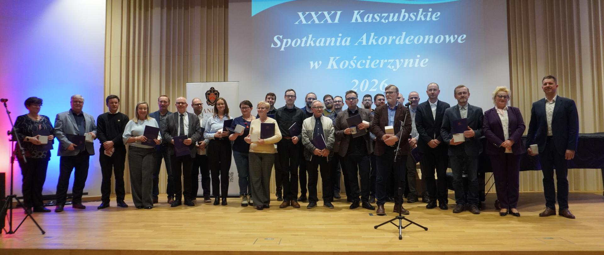 Na estradzie sali koncertowej kościerskiej szkoły muzycznej pozują w grupie na stojąco wszyscy nauczyciele, którzy przyjechali na konkurs wraz z uczniami