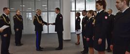 Pomorski komendant wojewódzki Państwowej Straży Pożarnej wspólnie ze swoimi zastępcami stojącymi za nim, wręcza medal funkcjonariuszowi. Obok stoją w rzędzie strażacy przewidziani do wyróżnień oraz awansów.