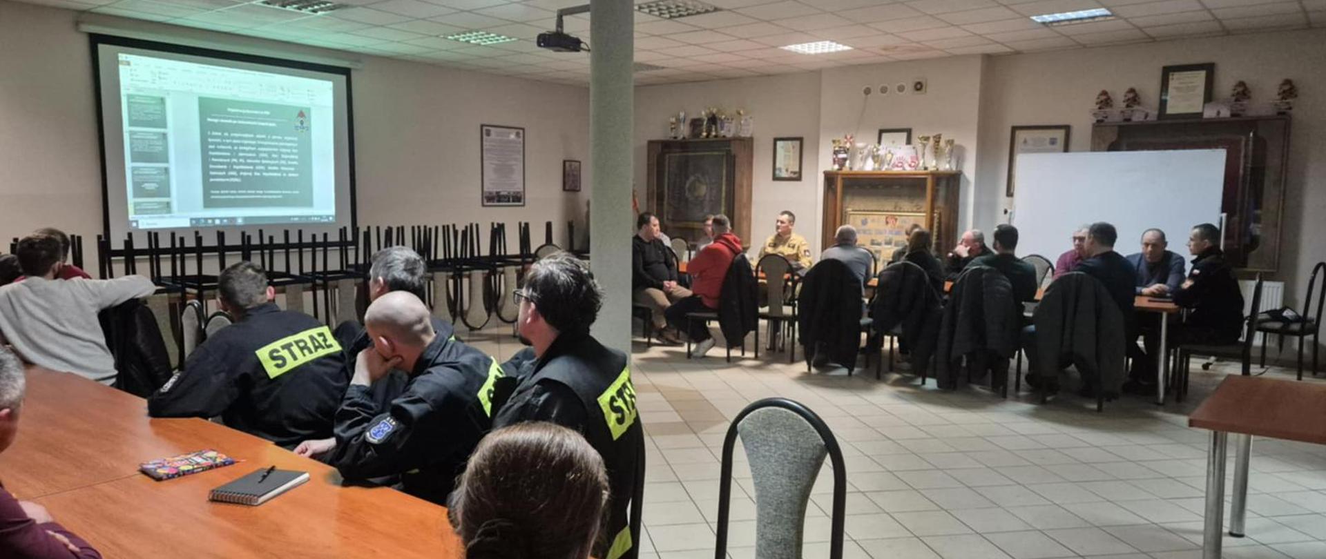 Na sali jednostki osp odbywa się szkolenie z łączności. Funkcjonariusz za pomocą prezentacji multimedialnej przekazuje wiedzę teoretyczną na temat omawianej dziedziny