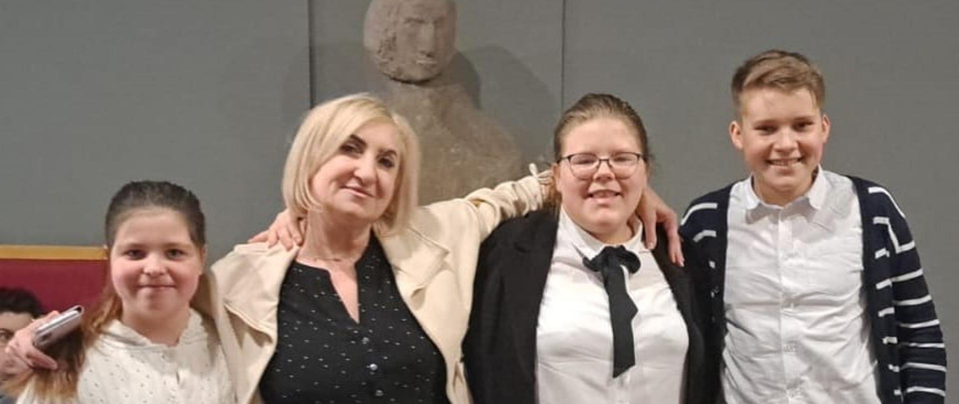 Na zdjęciu 3 uczniowie stoją ze swoją nauczycielką, z tyłu popiersie Chopina