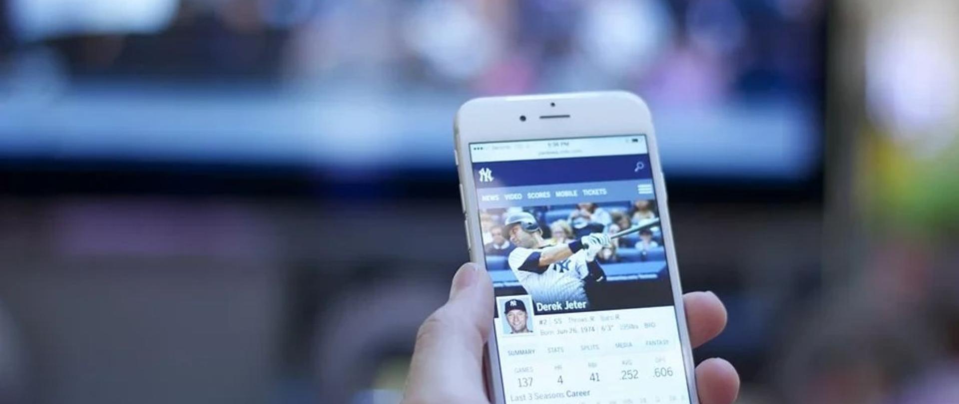 Ręka ze smartfonem, w tle ekran tv