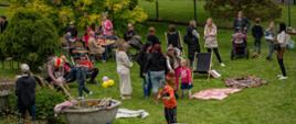 Zdjęcie przedstawia osoby uczestniczące w pikniku, który się odbył na ogrodzie przed budynkiem Studium. Na zielonej trawie rozłożone są koce. Stoją osoby dorosłe dzieci. 