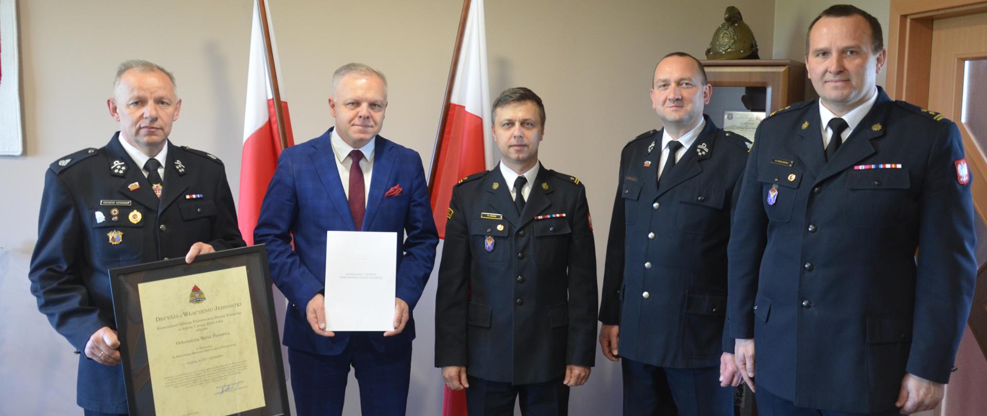 Zdjęcie przedstawia od lewej Prezesa OSP Kłobuck druha Krzysztofa Kotkowskiego trzymającego decyzję Komendanta Głównego Państwowej Straży Pożarnej włączającą jednostkę OSP Kłobuck do Krajowego Sytemu Ratowniczo-Gaśniczego obok Burmistrz Miasta i Gminy Kłobuck Pan Jerzy Zakrzewski, Komendant Powiatowy Państwowej Straży Pożarnej w Kłobucku mł. bryg. Karol Wers, Komendant Gminny ZOSP w Kłobucku druh Tomasz Cajler oraz Z-ca Komendanta Powiatowego bryg. Roman Królewski