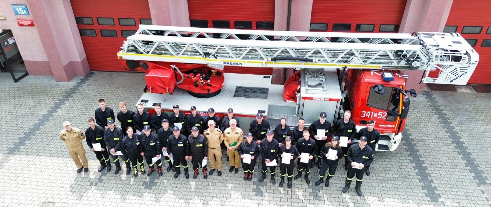 Strażacy stojący przed drabiną mechaniczną z zaświadczeniami z kursu