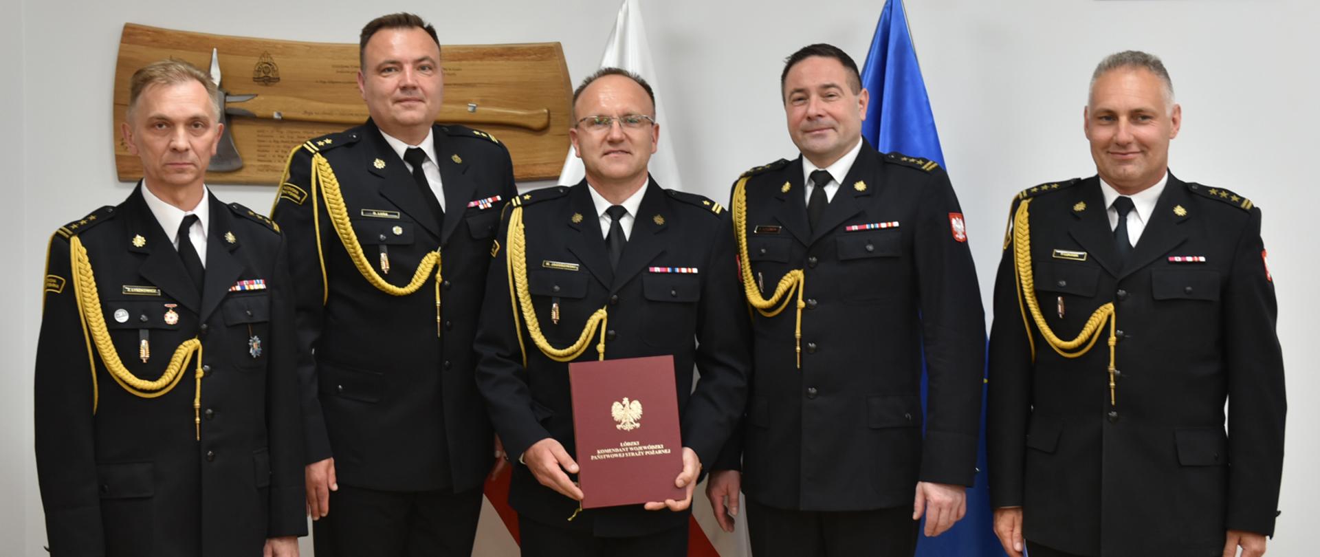 od lewej st. bryg. Zbigniew Łyszkowicz, bryg. Dariusz Lusa, mł. bryg. Mariusz Jagodziński, st. bryg. Sebastian Kościsty, st. bryg. Piotr Łukasik pozują do zdjęcia, za nimi na stojaku flaga Polski i Unii Europejskiej