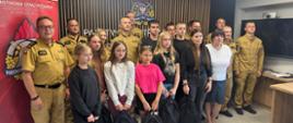"Wręczenie dyplomów i nagród laureatom ogólnopolskiego konkursu przez funkcjonariuszy Państwowej Straży Pożarnej w sali konferencyjnej Komendy Powiatowej w Zduńskiej Woli. Na zdjęciu widać uśmiechnięte dzieci odbierające upominki oraz strażaków w mundurach służbowych."
