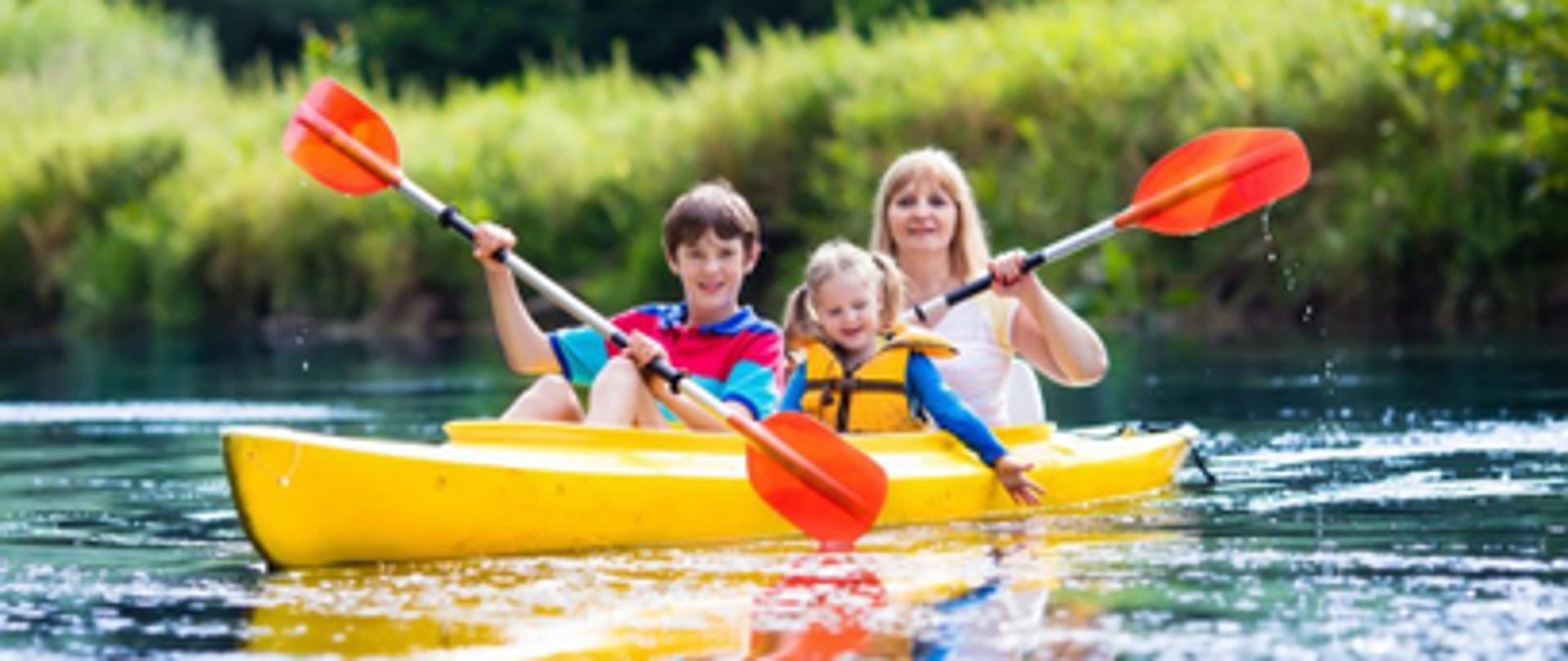 na zdjęciu jedna osoba dorosła i dwoje dzieci w wieku około sześć, osiem lat płyną kajakiem po jeziorze