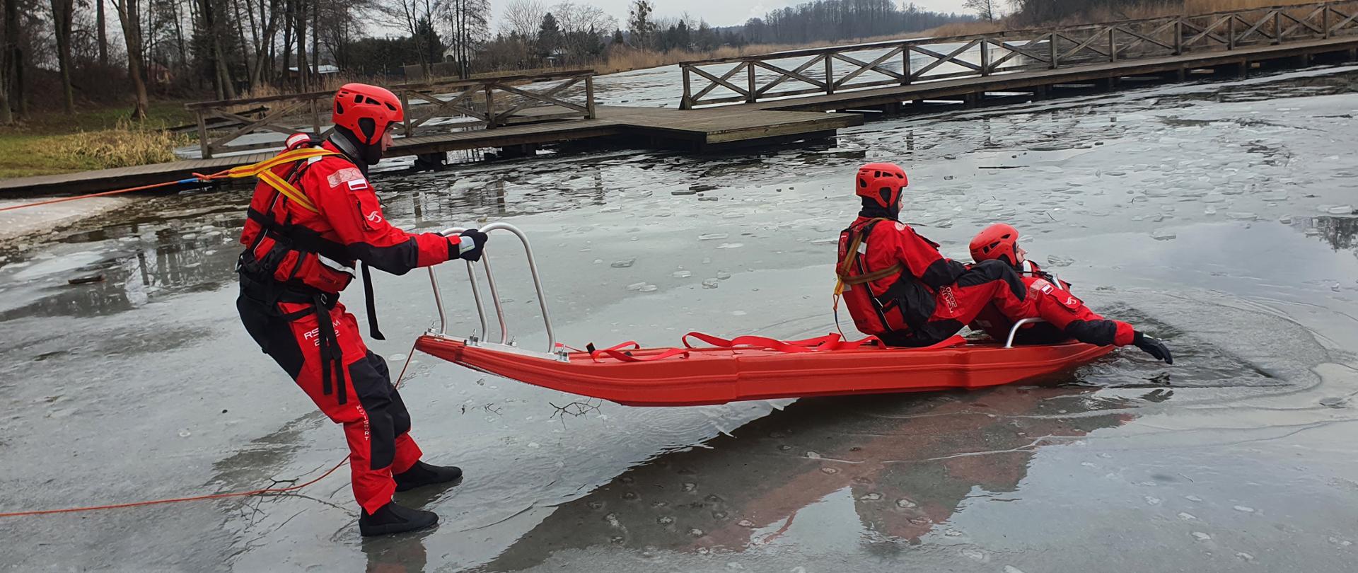 Strażacy przy użyciu sań lodowych wydobywają z wody pozoranta który wpadł do przerębla.