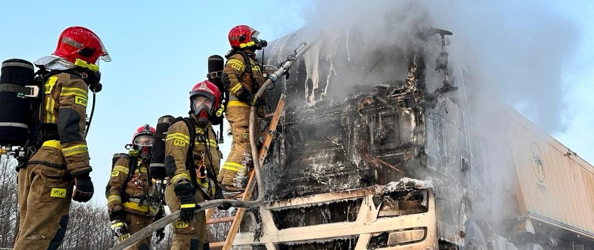 Strażacy z drabiny przystawnej dogaszają płonący samochód