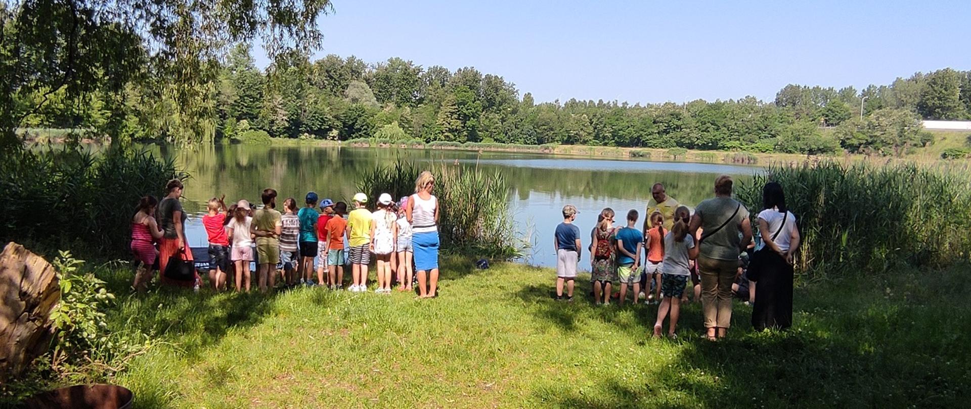 Zdjęcie przedstawia dzieci stojące przy stawie.
