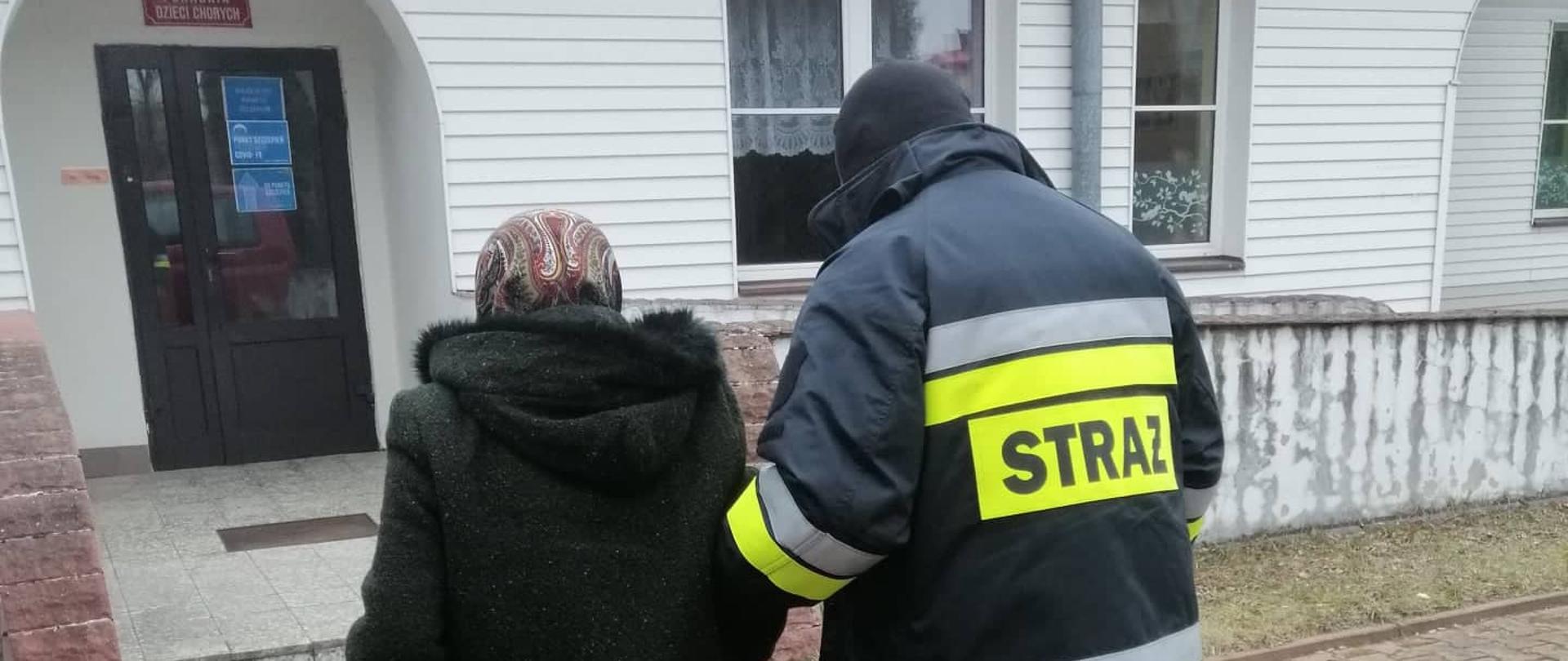 Strażak z OSP Krynki pomaga przejść do punktu szczepień starszej kobiecie