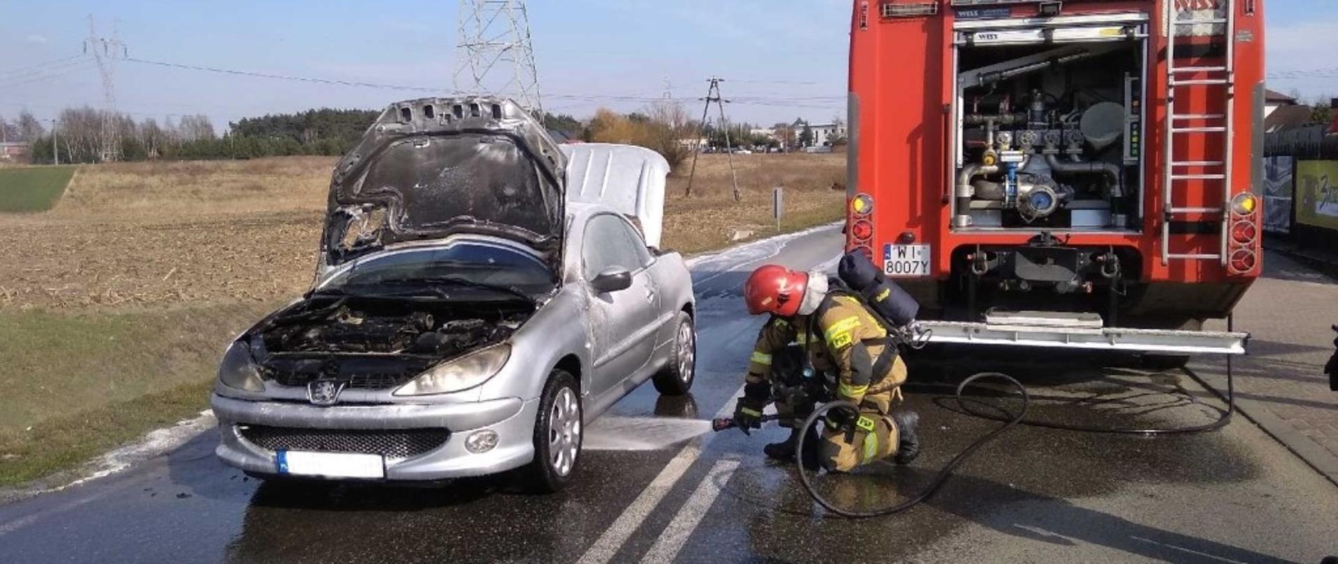 Strażak podaje prąd wody na samochód osobowy.