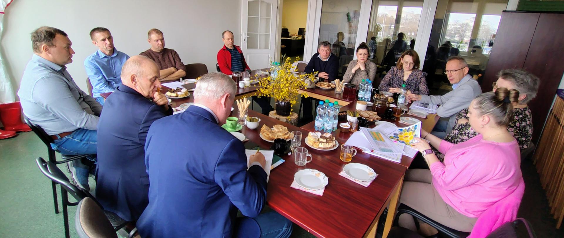 Uczestnicy spotkania siedzą przy wspólnym stole konferencyjnym w trakcie wystąpienia przedstawicielki inspekcji