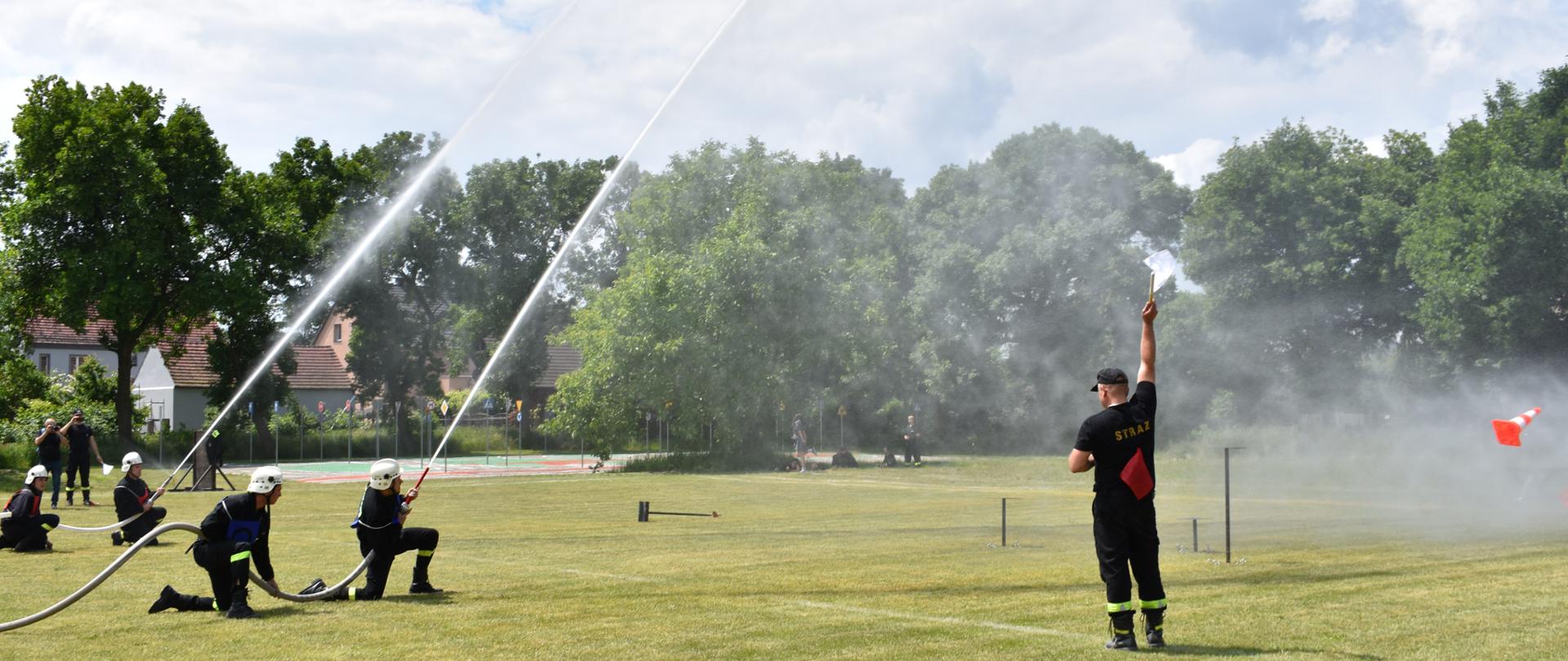 Na zdjęciu widoczni są strażacy podczas zawodów. Wykonują ćwiczenie bojowe. Na zdjęciu strażacy podczas strącania prądem wody tarczy oraz stożków.