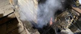Okopcony komin. Z komina wydobywa się dym. Częściowo rozebrany strop przy kominie.