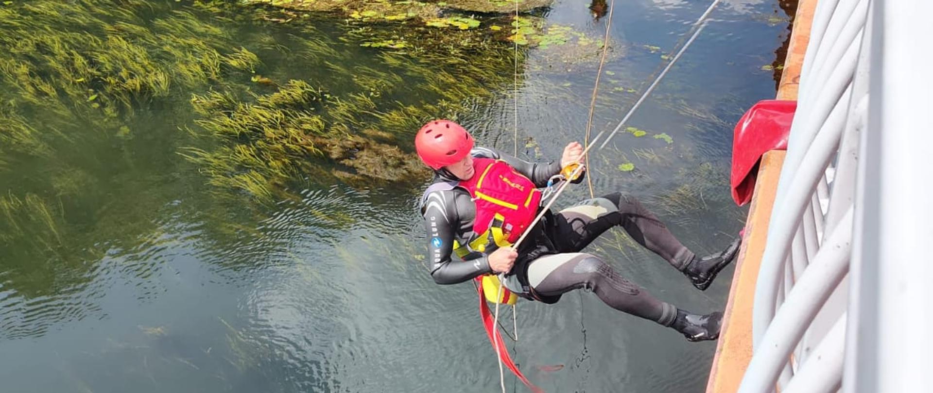 Na zdjęciu widnieją strażacy ćwiczący na obszarze wodnym-rzece wykorzystanie technik linowych. 