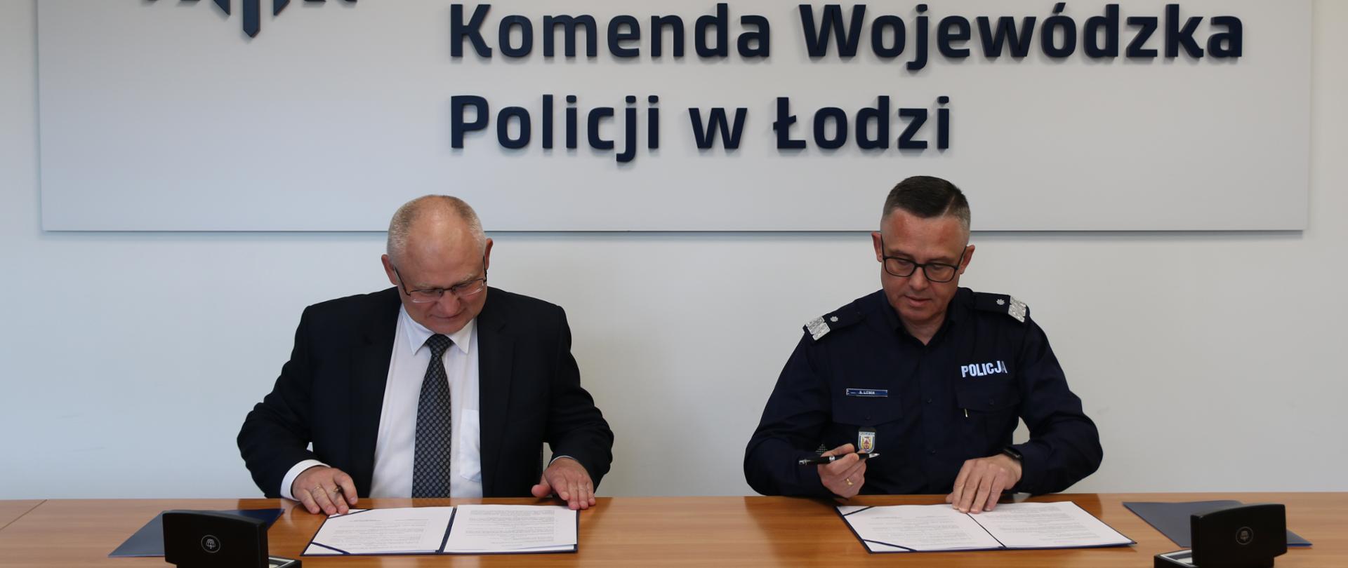 dwóch mężczyzn siedzi za stołem, mężczyzna z lewej strony zdjęcia ubrany jest garnitur, mężczyzna z prawej strony zdjęcia ubrany jest w mundur z widocznym napisem Policja, nad nimi widoczny napis Policja Komenda Wojewódzka Policji w Łodzi 