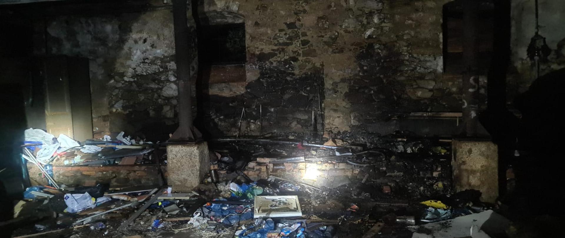 Pomieszczenie w którym wybuchł pożar, częściowo oświetlone przez latarki. Duże nagromadzenie śmieci.