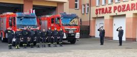 Zdjęcie przedstawia strażaków podczas uroczystego podniesienia flagi państwowej na palcu Komendy.
W tle budynek komendy.
