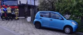 Samochód osobowy stoi na poboczu a za nim strażacy i samochód pożarniczy.