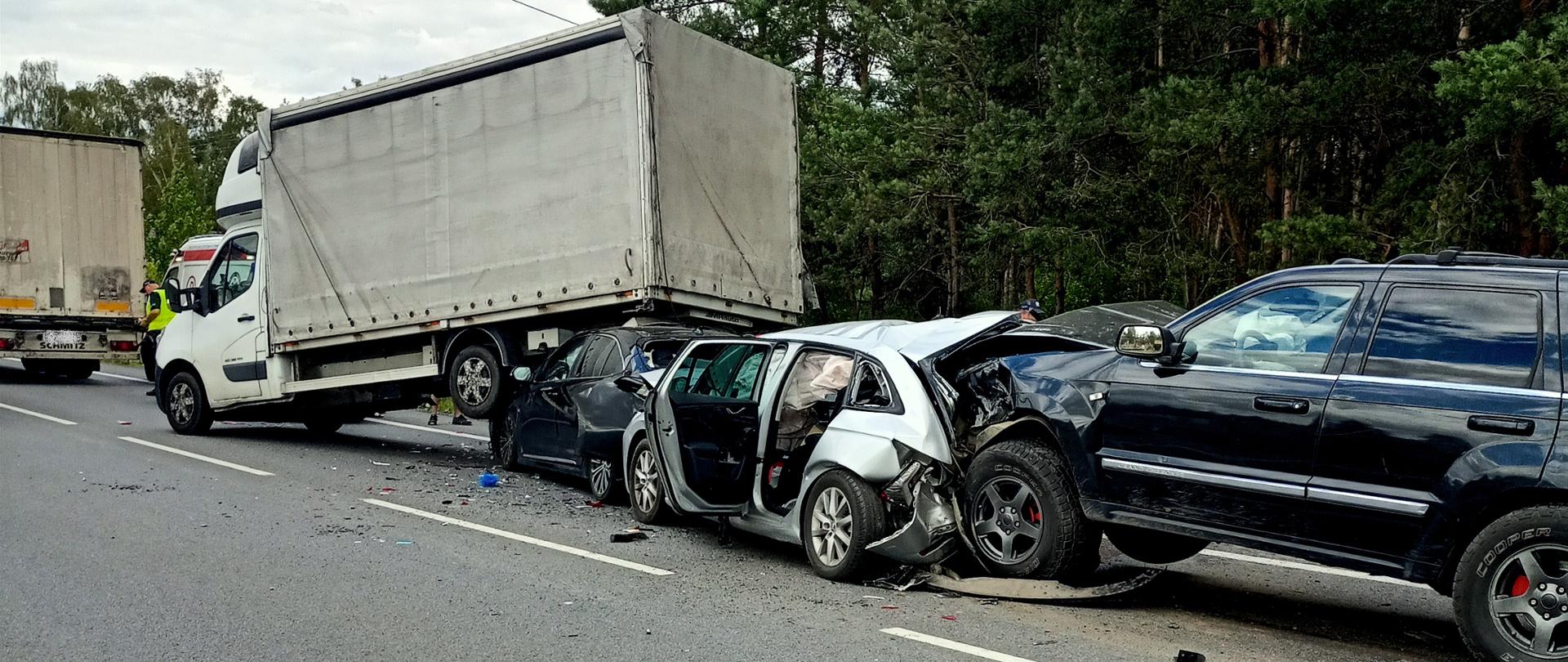 Zdjęcie przedstawia wypadek z udziałem czterech samochodów osobowych oraz samochodu dostawczego. Jeden samochód osobowy wjechał pod tył samochodu dostawczego, Kolejne samochody uderzały w tył. 