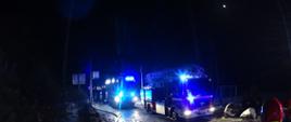 Zdjęcie przedstawia dwa pojazdy ratowniczo- gaśnicze podczas pożaru. Na zdjęciu widoczne dwie linie gaśnicze oraz strażaka który koordynuje działania. Zdjęcie wykonane w porze nocnej.