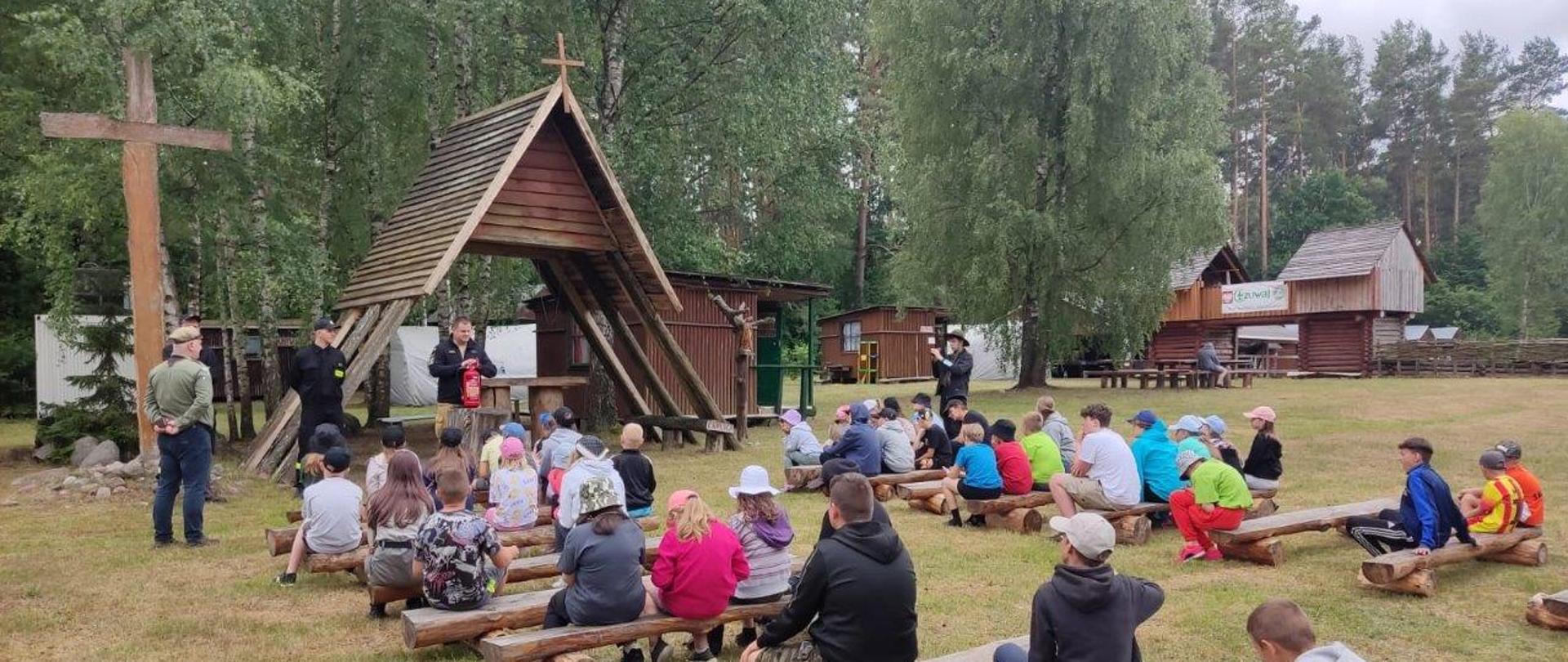 Dzieci siedzą na ławkach przed ołtarzem polowym