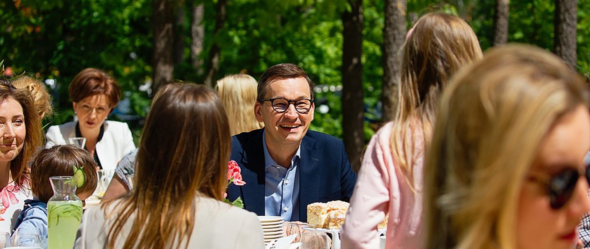 Premier siedzi i rozmawia z dzieckiem.