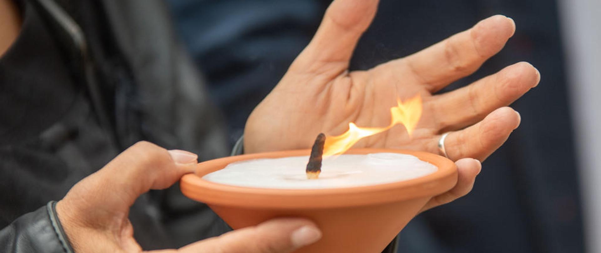 Międzynarodowy Dzień Pamięci o Zagładzie Romów a w tle w dłoniach trzyma zapalony znicz