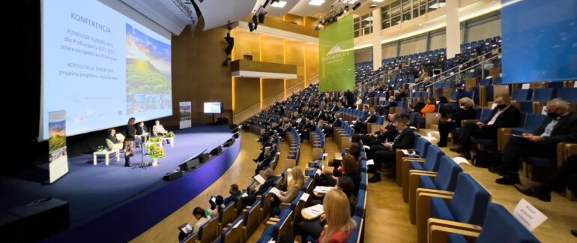 Uczestnicy konferencji dotyczącej konsultacji Fundusze Europejskie dla Podkarpacia słuchają przemówienie wojewody podkarpackiego Ewy Leniart. 