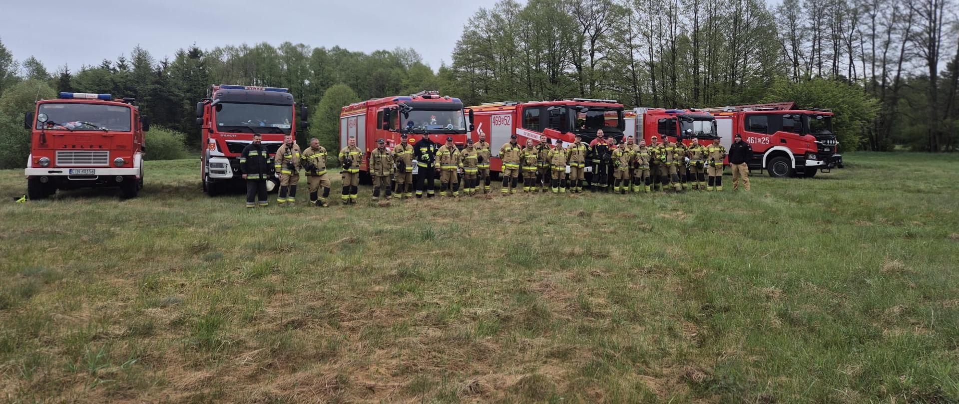 Strażacy biorący udział w ćwiczeniach na tle samochodów gaśniczych