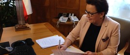 Anna Zalewska podpisuje dokumenty przy biurku