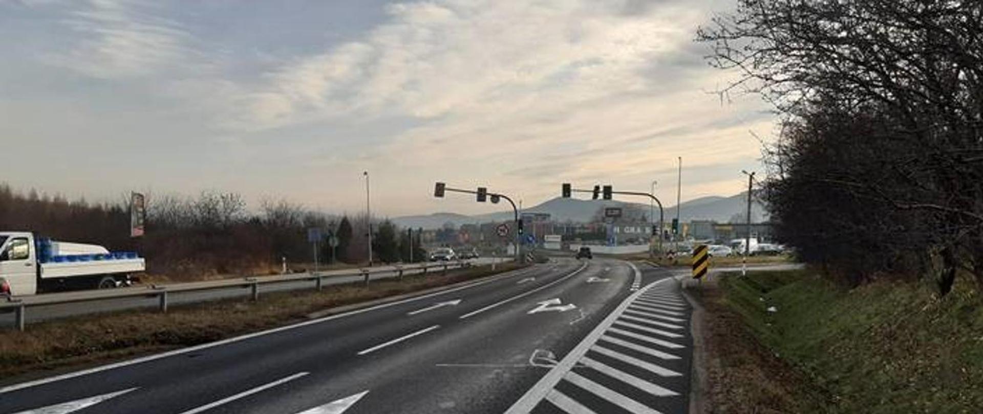 Zdjęcie DK7 w Myślenicach. Dwie jezdnie po dwa pasy ruchu z widocznym oznakowaniem poziomym. W oddali skrzyżowanie z sygnalizacją świetlną