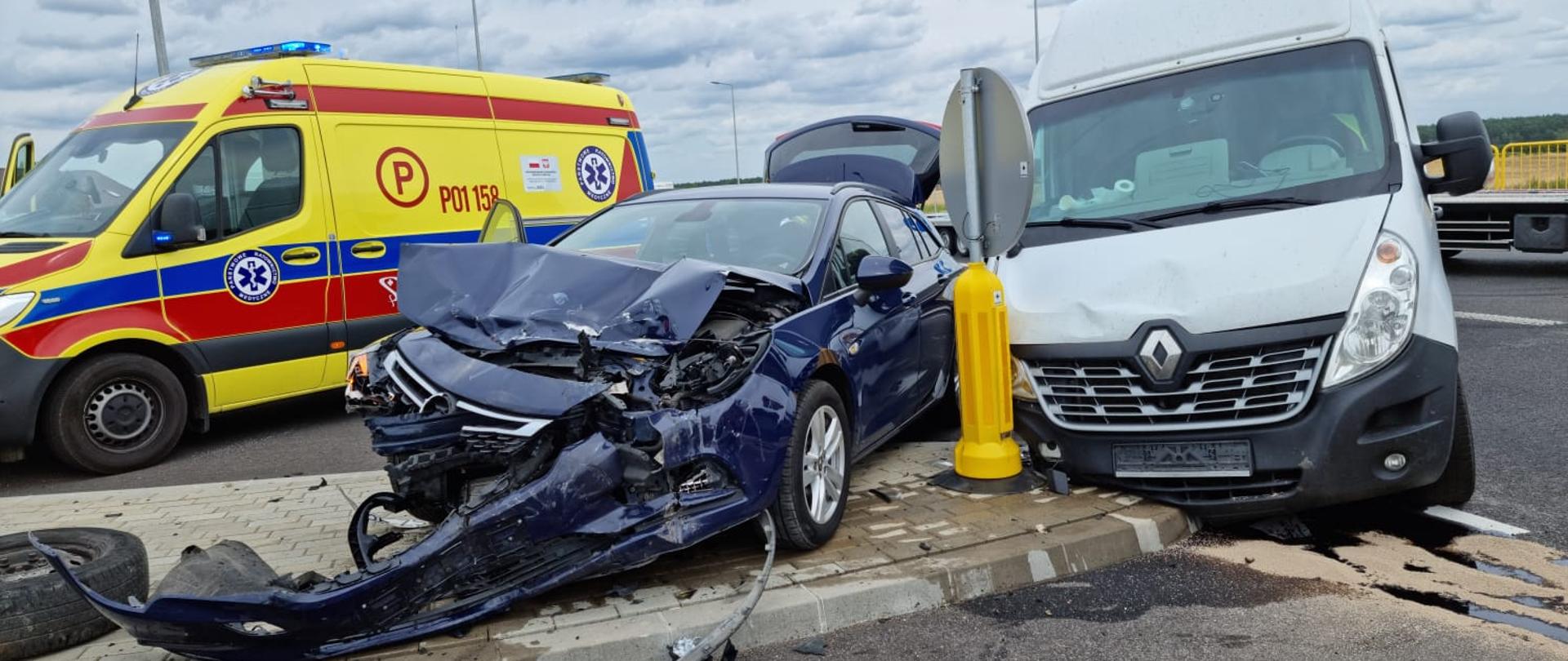Widać dwa uszkodzone samochody na środku skrzyżowania, po lewej stronie jest kartka pogotowia