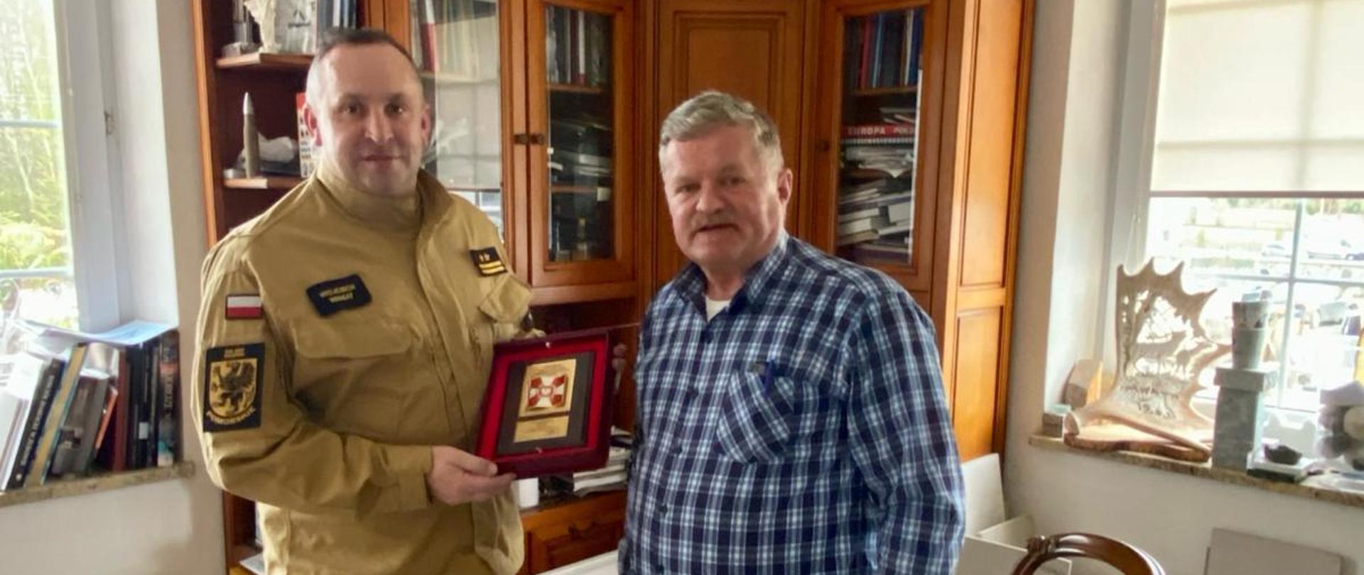 Komendant Powiatowy PSP w Pucku Pan bryg. Wojciech Wanat wręcza pamiątkowy grawerton właścicielowi firmy MURKAM Panu Leonowi Czerwińskiemu. Komendant ma na sobie ubranie służbowe w kolorze piaskowym. Zdjęcie wykonane w siedzibie firmy Murkam.