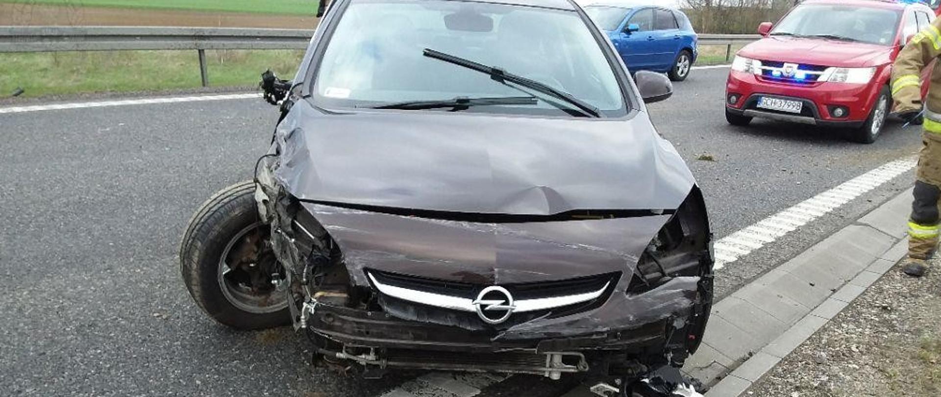 Rozbity przód samochodu osobowego w ciemnym kolorze na pasie jezdni obwodnicy Chojnic. 