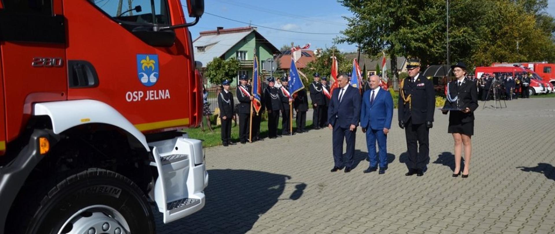 Na zdjęciu po lewej kabina nowego samochodu ratowniczo-gaśniczego przekazywanego jednostce OSP Jelna. Dalej zaproszeni goście (wśród nich nadbrygadier Andrzej Babiec) gotowi do uroczystego przekazania kluczyków do pojazdu.