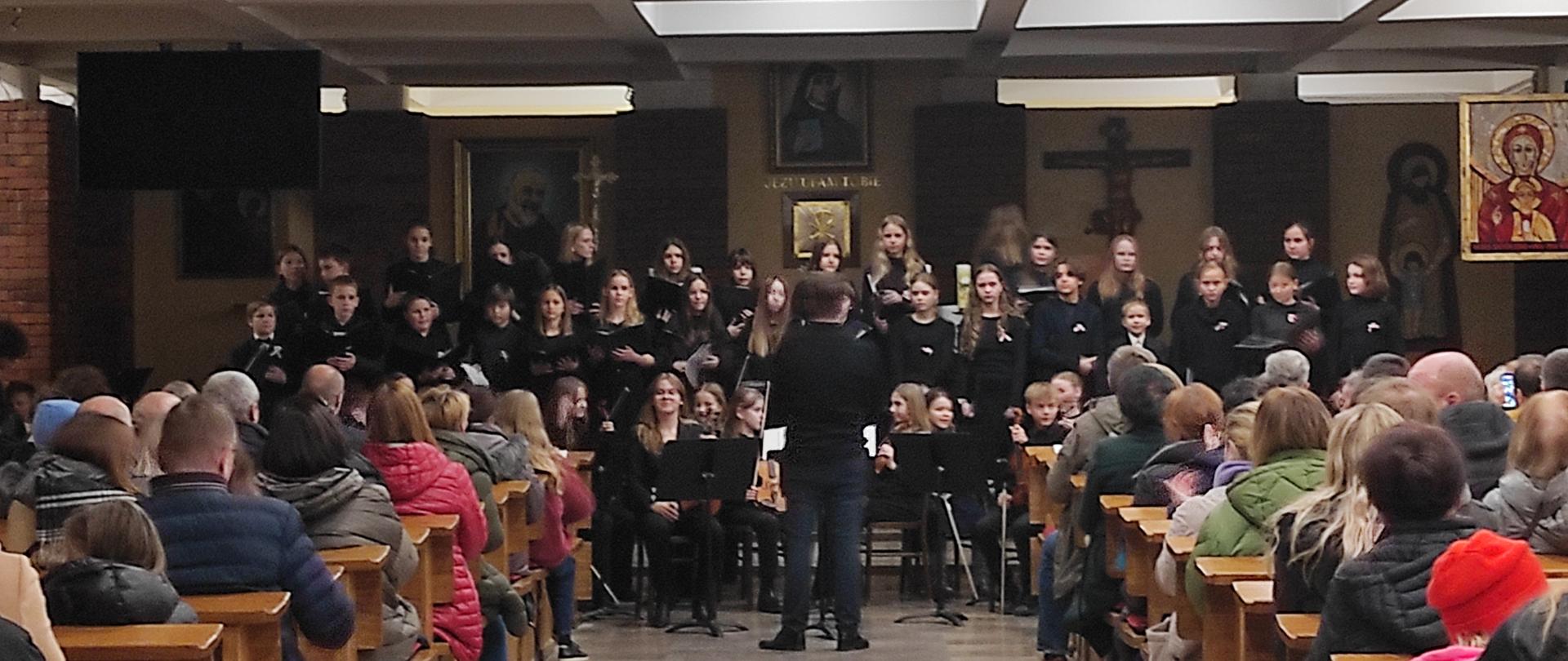 chór i orkiestra uczniów pod dyrekcją nauczyciela podczas koncertu